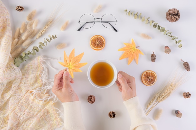 Vrouw met esdoornblad en kopje thee over herfst achtergrond.