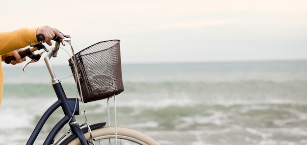 Vrouw met fiets en gele trui, zee met golven op de achtergrond, gedeeltelijk zicht, ruimte voor tekst.