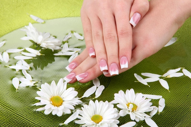 Vrouw met Franse manicure en bloemen in een groene kom met water.