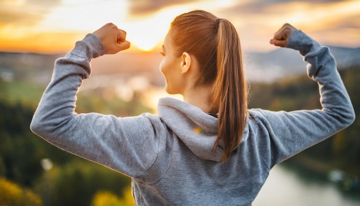 Foto vrouw met gebogen biceps die naar de zonsopgang kijkt als symbool van motivatie en empowerment.