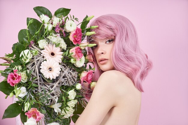 Vrouw met gekleurd roze sterk haar houdt een boeket prachtige bloemen in haar handen. Natuurlijk geverfd haar mooie make-up