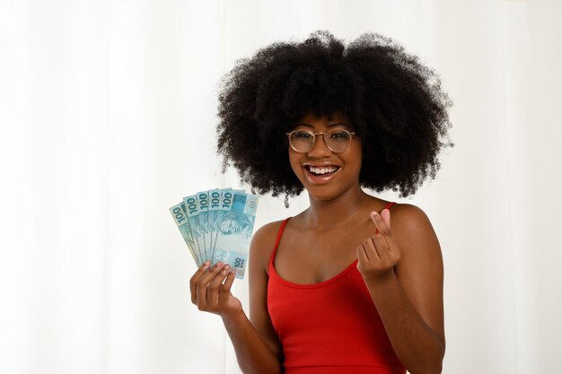 Vrouw met geld glimlachend zwart meisje met Braziliaanse bankbiljetten positief verrast gebaren