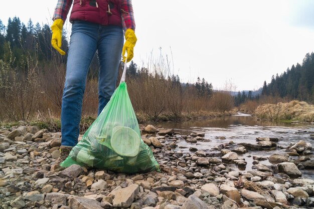 Vrouw met gele handschoenen die plastic afval verzamelen in de buurt van het bos van de rivier en de bergen concept van milieubescherming recycle project buiten ruimte kopiëren