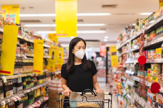 Vrouw met gezichtsmasker die boodschappen in de supermarkt draagt tijdens quarantaine van het coronavirus