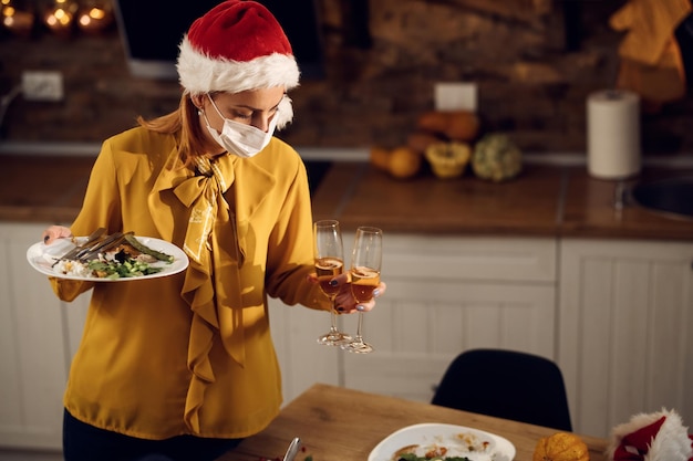 Vrouw met gezichtsmasker die eetkamer schoonmaakt na een maaltijd met Kerstmis