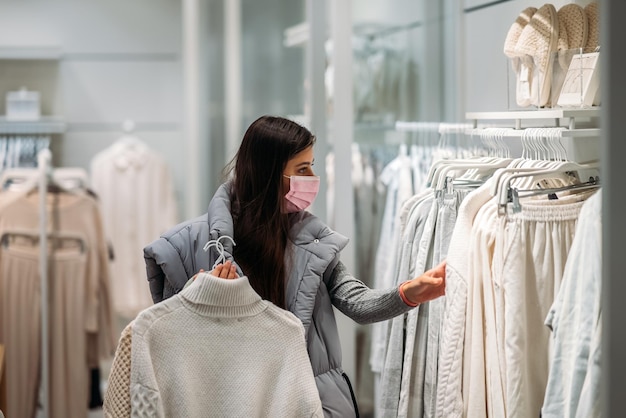 Vrouw met gezichtsmasker kiest kleding in kledingwinkel