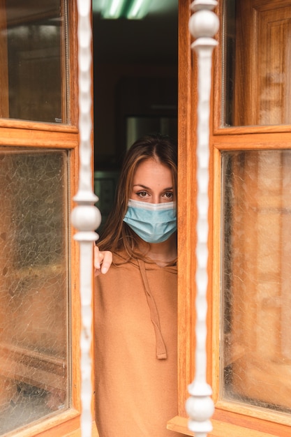 vrouw met gezichtsmasker kijkt uit het raam