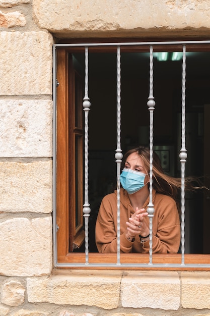 Foto vrouw met gezichtsmasker klappen bij het raam