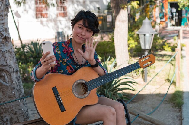 Vrouw met gitaar die een videogesprek voert terwijl ze in een park zit