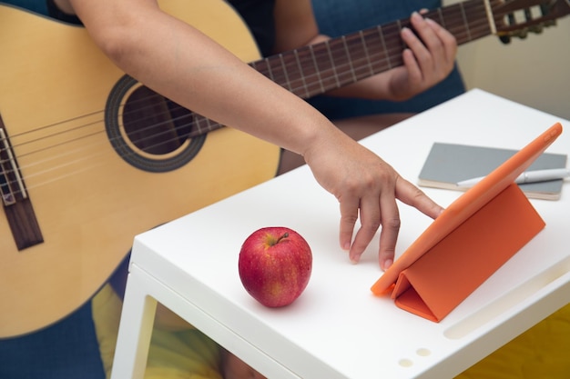 Vrouw met gitaar die thuis controleert op online les, muziekbladen op digitale tablet