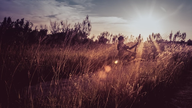 Foto vrouw met gitaar in het grasveld bij zonsondergang