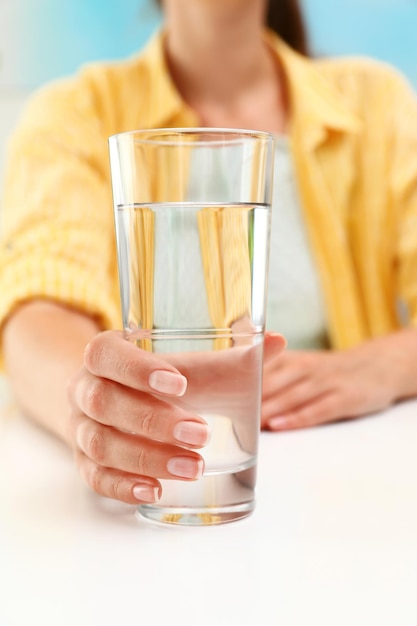 Vrouw met glas water aan witte tafel close-up Verfrissend drankje