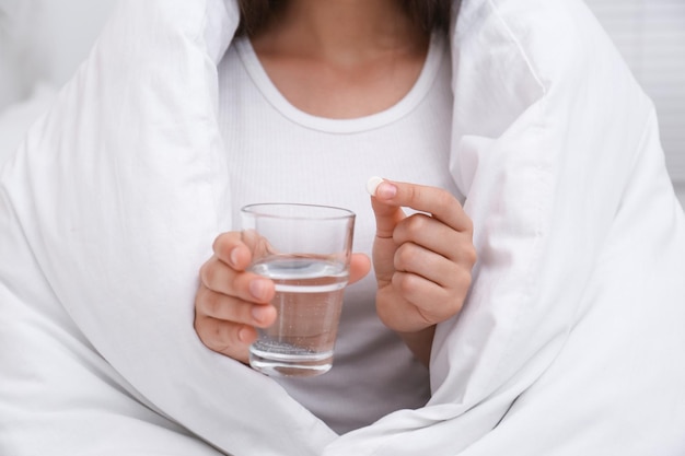 Vrouw met glas water en pil in slaapkamer close-up