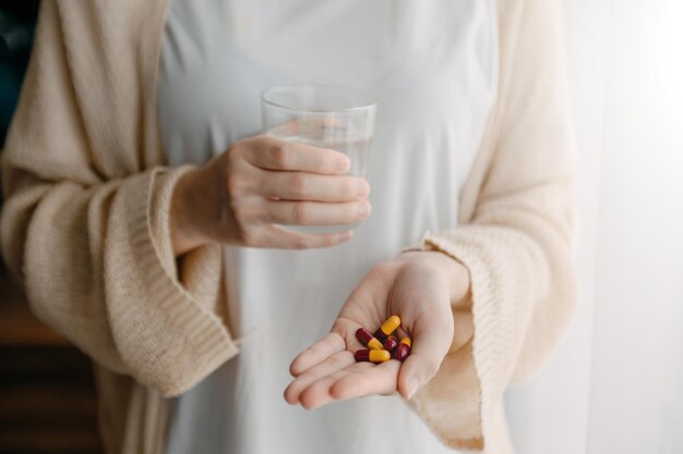 Vrouw met glas water en pillen bij de hand die medicijnen gaan nemen die door zijn arts in huis zijn voorgeschreven