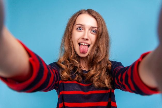 Vrouw met grappige gezichtsuitdrukking die selfie neemt en tong uit het gezichtspunt van foto laat zien