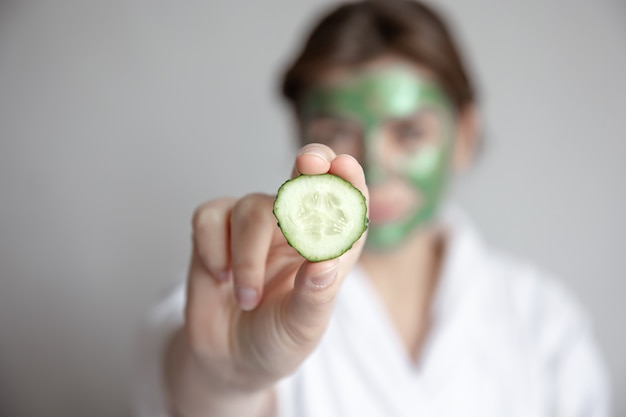 Vrouw met groen masker op haar gezicht met verse komkommerplak, vage achtergrond, concept van schoonheid en gezondheid van de gezichtshuid.