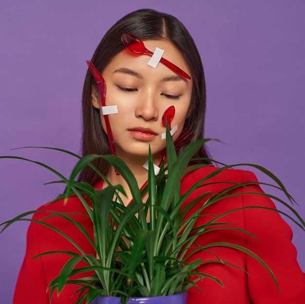 Foto vrouw met haar gezicht bedekt met plastic lepels terwijl ze een plant vasthoudt