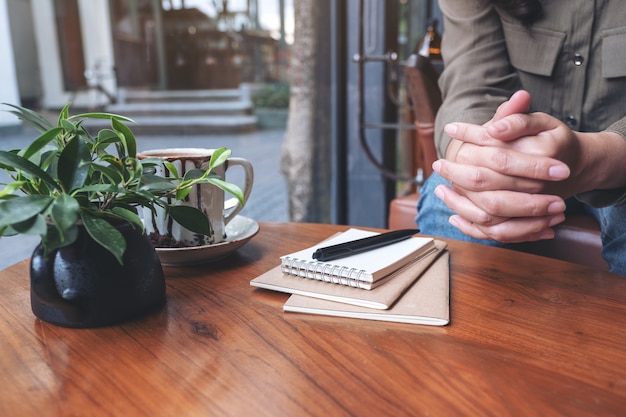 Vrouw met haar handen zittend in het huis met notebooks, pen en koffiekopje op houten tafel