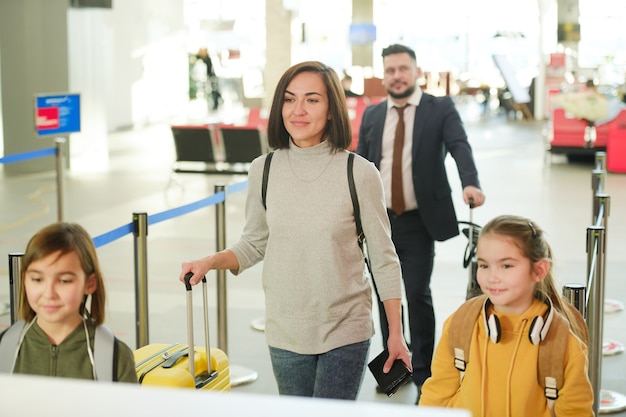 Vrouw met haar kinderen die op vakantie gaan, ze staan in de rij en wachten op vertrek op de luchthaven