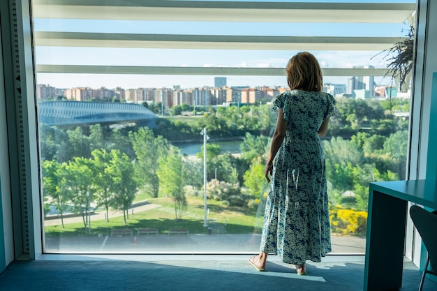 Vrouw met haar rug en staand genietend van het uitzicht op de stad vanuit een groot raam Zaragoza Spanje