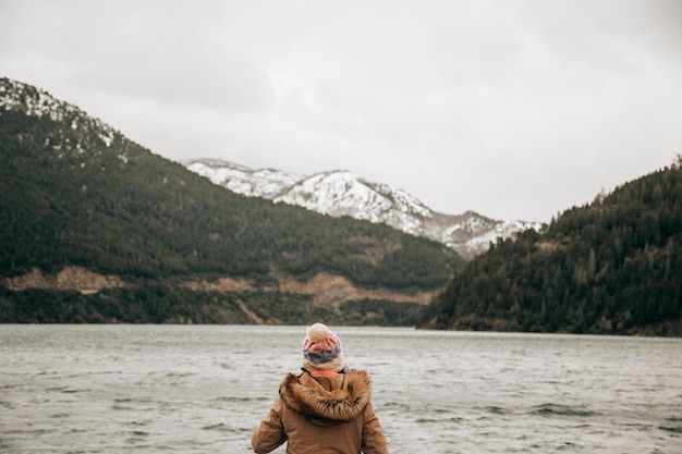 Vrouw met haar rug naar een meer met besneeuwde bergen