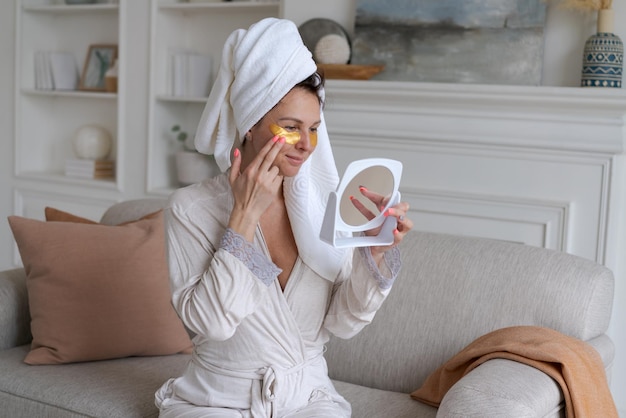 Vrouw met handdoek op haar hoofd kijkt in de spiegel en brengt gouden pleisters aan
