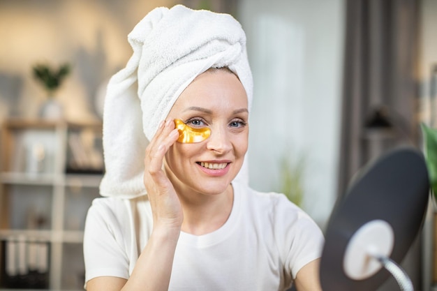 Vrouw met handdoek op het hoofd die thuis ooglapjes gebruikt