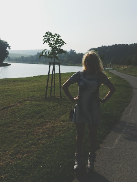 Foto vrouw met handen op de heup staat aan de oever van het meer tegen de lucht