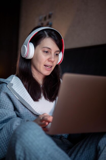 Vrouw met headset die op laptop werkt, heeft een videogesprek op afstand vanuit huis