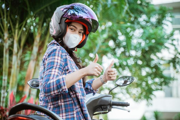 Vrouw met helm en masker met twee duimen omhoog op motor langs de weg