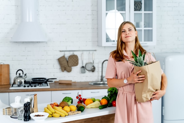 Vrouw met het kruidenierswinkelpakket in de handen. Keuken achtergrond. Jonge vrouw met gezond voedsel.