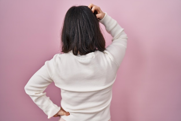 Vrouw met het syndroom van down die over een roze achtergrond staat en achterwaarts nadenkt over twijfel met de hand op het hoofd