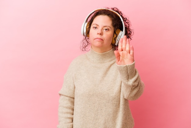 Vrouw met het syndroom van down met hoofdtelefoons die op roze achtergrond wordt geïsoleerd die zich met uitgestrekte hand bevindt die stopbord toont, dat u verhindert.