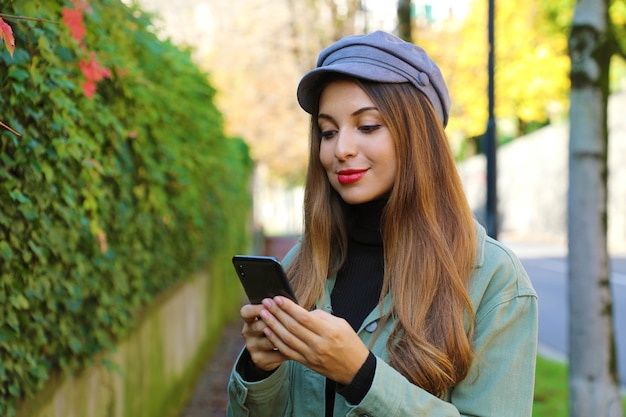 Vrouw met hoed en jasje messaging met mobiele telefoon buitenshuis