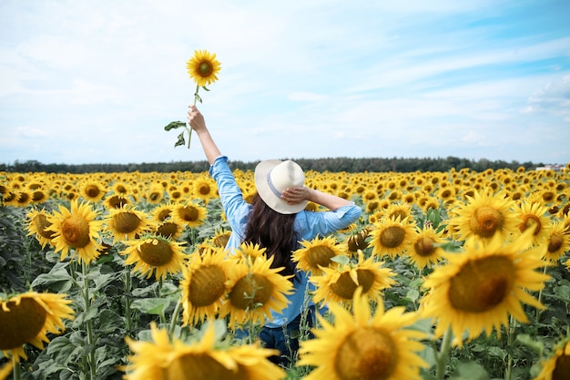 Vrouw met hoed in zonnebloemenveld genietend van de natuur