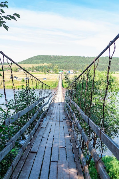 Vrouw met hond loopt langs de oude houten hangbrug over de rivier in zonnige zomerdag. Natuurlijk landschap. Hond op brug