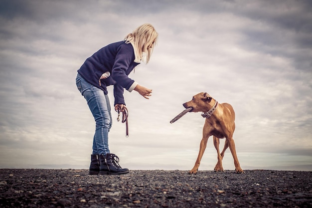 Vrouw met hond op het veld tegen bewolkte lucht