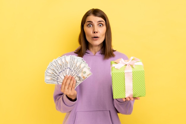 Vrouw met ingepakte huidige doos en doolars bankbiljetten kijkend naar de camera met open mond