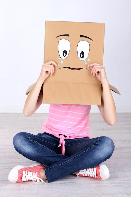 Foto vrouw met kartonnen doos op haar hoofd met droevig gezicht bij de muur