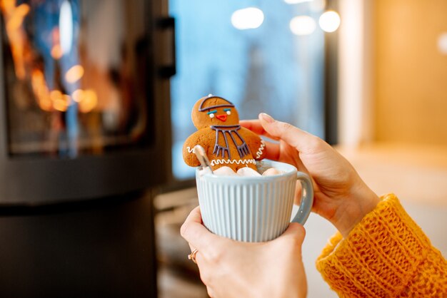 Vrouw met kerst peperkoek met kopje bij de open haard thuis