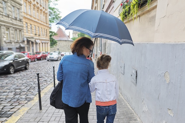 Vrouw met kindmeisje die onder een paraplu in straat lopen