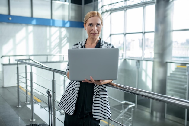 Vrouw met koffer en opengeklapte laptop staande op de luchthaven