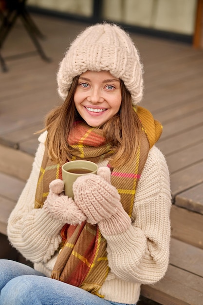 Vrouw met koffie zittend op veranda camera kijken