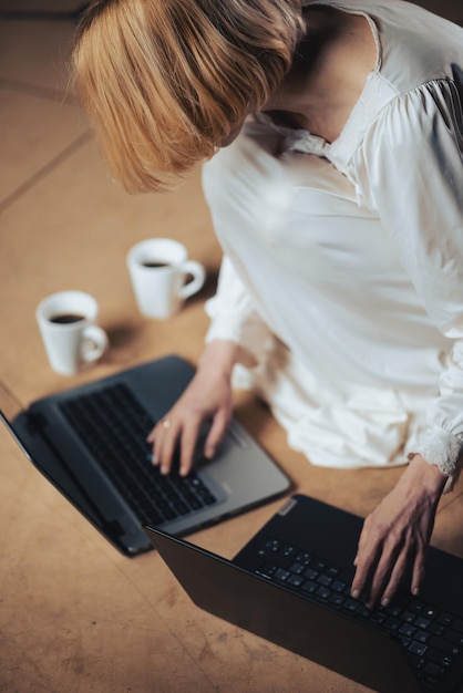 Vrouw met koffiekopjes voor twee laptops Deadline herwerken multitasking hard werken freelancer concept