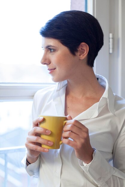 Vrouw met kop koffie die uit het raam kijkt