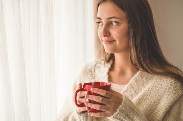 Vrouw met kop warme drank bij het raam