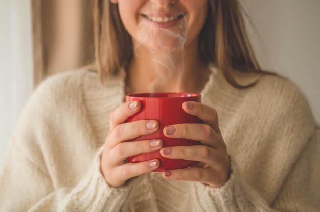 Vrouw met kop warme drank bij het raam