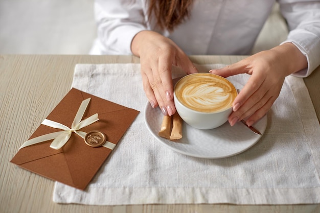 Vrouw met kopje cappuccino op tafel in café en cadeaubon uitnodiging envelop