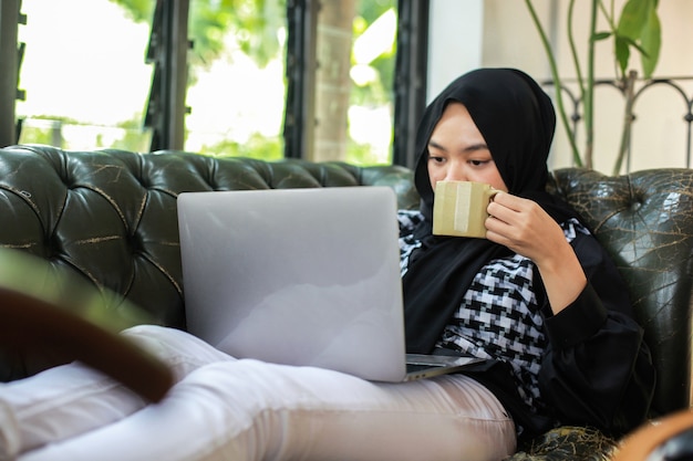 vrouw met kopje en laptop kijken terwijl u ontspant op de bank