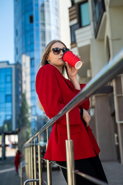 Vrouw met kopje koffie praat op haar smartphone terwijl ze midden in het stadscentrum staat